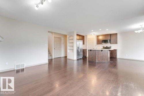 Spacious living area featuring wood-finish flooring, a kitchen island, stainless steel appliances, dark wood cabinetry, and recessed lighting - 16315 55 Street, Edmonton, AB 