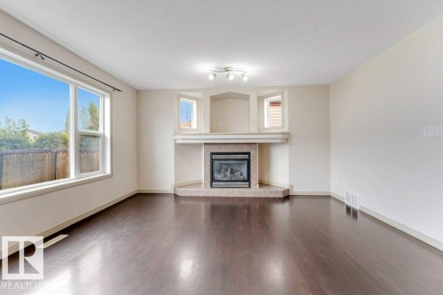 Spacious interior featuring dark wood-finish flooring and a corner fireplace with a tiled hearth and mantel - 16315 55 Street, Edmonton, AB 