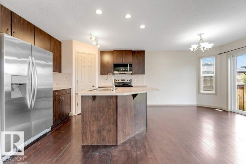 Open-concept kitchen featuring dark wood cabinetry, stainless steel appliances, a center island with a sink, light-colored countertops, and wood-finish flooring - 16315 55 Street, Edmonton, AB 
