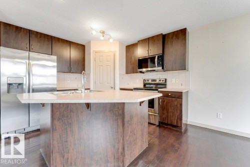Kitchen featuring dark wood-finish cabinetry, stainless steel appliances, a light-toned countertop, and a center island with a built-in sink - 16315 55 Street, Edmonton, AB 