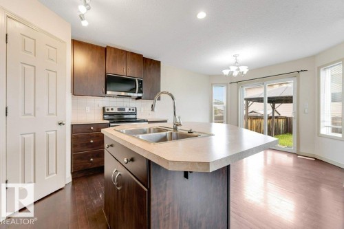 Kitchen featuring wood-finish flooring, dark wood cabinetry, a stainless steel microwave, a dual basin sink, and a breakfast bar island - 16315 55 Street, Edmonton, AB 