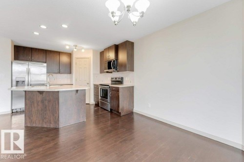Open-concept kitchen featuring an island with a sink, stainless steel appliances, dark wood-finish cabinetry, light countertops, and wood-finish flooring - 16315 55 Street, Edmonton, AB 