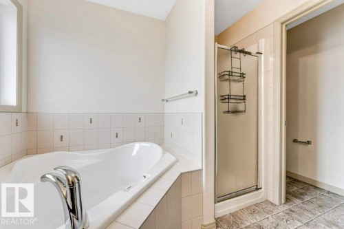 Built-in soaking tub with chrome fixtures, surrounded by white tile and a frosted glass window - 16315 55 Street, Edmonton, AB 