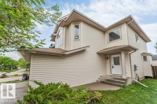 Cream-colored siding exterior featuring multiple bay windows, an elevated entry with steps, a covered porch, and mature landscaping - 16315 55 Street, Edmonton, AB 