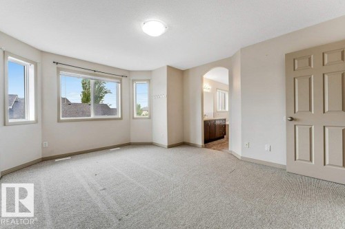 Spacious room featuring light-colored carpeting, multiple windows, a six-panel interior door, and an arched doorway leading to a bathroom with a wood-finish vanity - 16315 55 Street, Edmonton, AB 