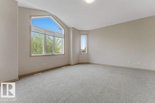 Spacious room featuring a large geometric window, neutral-toned carpeting, light beige wall paint, and a ceiling-mounted light fixture - 16315 55 Street, Edmonton, AB 