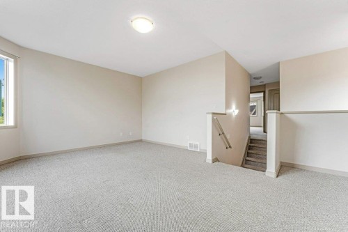 Spacious room with light neutral wall tones, textured carpet flooring, and a large window providing natural illumination - 16315 55 Street, Edmonton, AB 