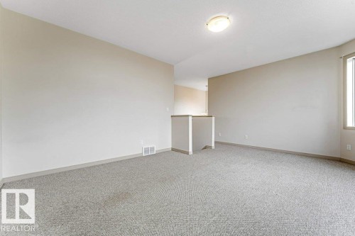 Spacious room featuring neutral wall tones, light-colored textured carpet, and a flush-mount ceiling light fixture - 16315 55 Street, Edmonton, AB 