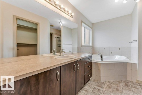 Bathroom featuring a dual vanity with integrated sinks, a built-in corner soaking tub, and a window for natural light - 16315 55 Street, Edmonton, AB 