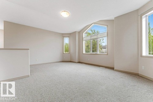 Bright, carpeted room featuring a large central arched window, additional tall vertical windows, and neutral wall tones - 16315 55 Street, Edmonton, AB 