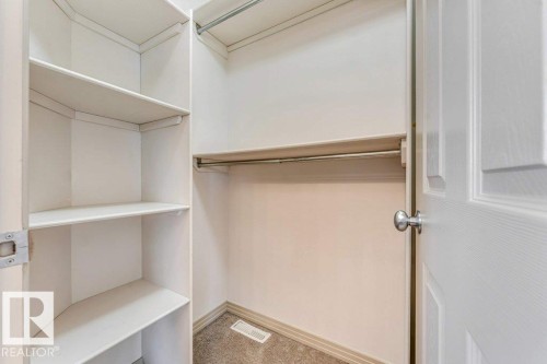 Walk-in closet featuring built-in shelving, two clothing rods, light beige walls, and carpet flooring - 16315 55 Street, Edmonton, AB 