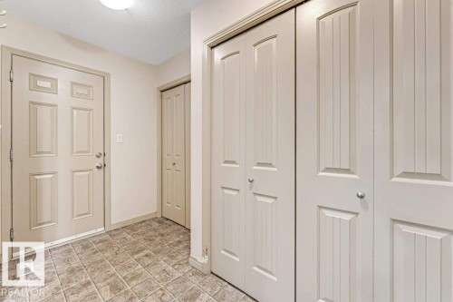 Foyer featuring paneled entry door, bi-fold closet doors, textured ceiling, and tile flooring - 16315 55 Street, Edmonton, AB 