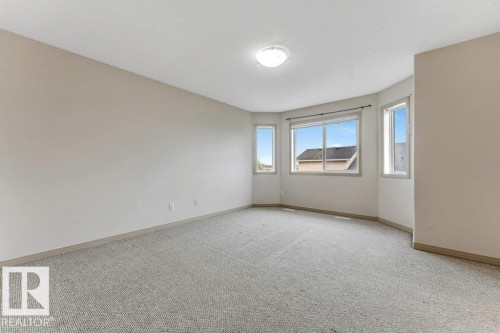 Spacious room featuring neutral carpeting, light-toned wall finishes, and a multi-window bay with natural light - 16315 55 Street, Edmonton, AB 