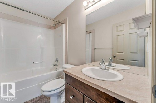 Bathroom featuring a wood-finish vanity with a light-toned countertop, oval undermount sink, and polished chrome faucet - 16315 55 Street, Edmonton, AB 