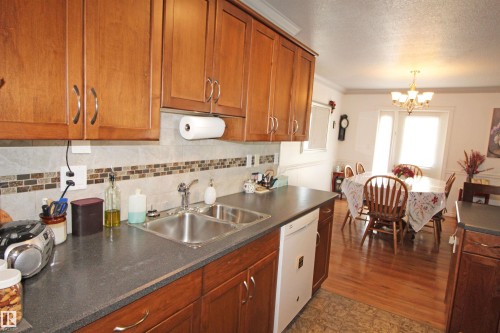 Kitchen featuring wood cabinetry, a double basin stainless steel sink, and a tiled backsplash with decorative accents - 334 7001 Northview Drive, Wetaskiwin, AB - Indoor Photo Showing Kitchen With Double Sink