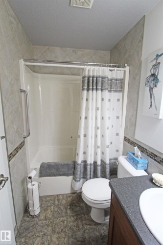 White bathtub and shower combination with a grab bar, surrounded by tiled walls with a mosaic accent strip - 334 7001 Northview Drive, Wetaskiwin, AB - Indoor Photo Showing Bathroom