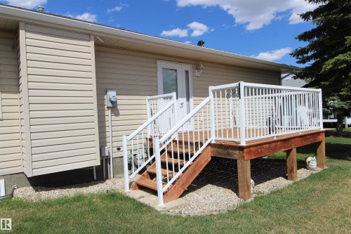 Rear wood-finish deck with white railings and staircase, featuring double French doors, light beige siding, and a gravel base - 334 7001 Northview Drive, Wetaskiwin, AB - Outdoor With Deck Patio Veranda With Exterior