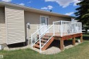 Rear wood-finish deck with white railings and staircase, featuring double French doors, light beige siding, and a gravel base - 334 7001 Northview Drive, Wetaskiwin, AB  - Outdoor With Deck Patio Veranda With Exterior 