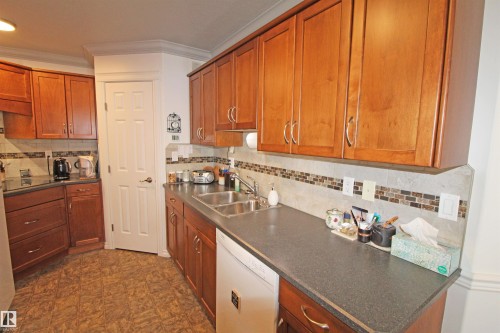 Kitchen featuring wood cabinetry, dark countertops, a mosaic tile backsplash, and a double basin sink - 334 7001 Northview Drive, Wetaskiwin, AB - Indoor Photo Showing Kitchen With Double Sink