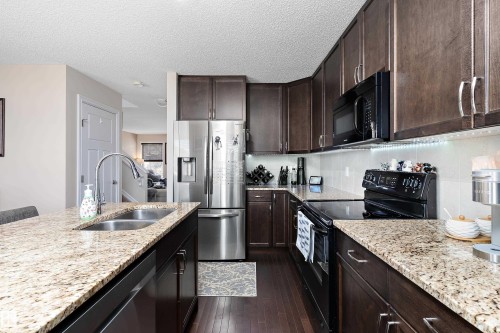 Kitchen featuring granite countertops, dark wood-finish cabinetry, stainless steel refrigerator, and integrated black appliances - 6822 Cardinal Link, Edmonton, AB 