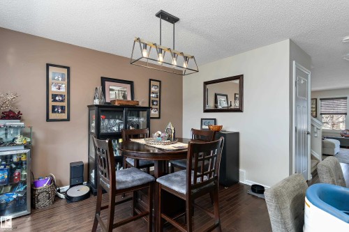 Dining area featuring wood-finish flooring, a modern linear chandelier with exposed bulbs, and a two-tone wall color scheme - 6822 Cardinal Link, Edmonton, AB 
