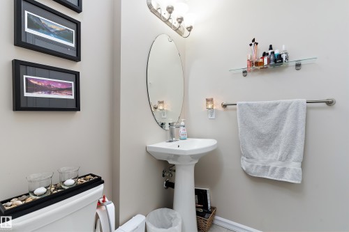 White pedestal sink with an oval mirror and brushed nickel vanity lighting - 6822 Cardinal Link, Edmonton, AB 