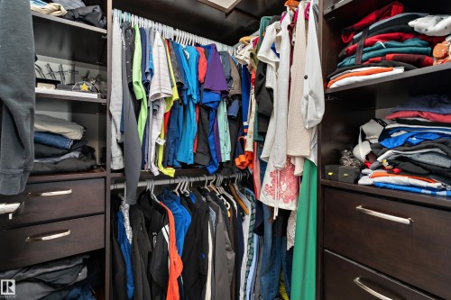 Custom closet system featuring dark wood-finish cabinetry, ample hanging space, integrated shelving, and multiple storage drawers with brushed nickel hardware - 6822 Cardinal Link, Edmonton, AB 