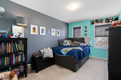 Carpeted bedroom featuring two distinct wall colors, a wood-finish bed frame with integrated storage drawers, and two windows with blinds - 6822 Cardinal Link, Edmonton, AB 