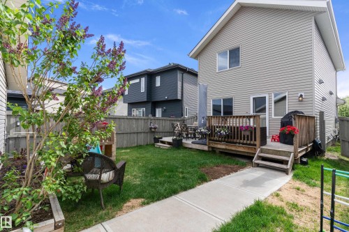 Backyard featuring a wood deck, concrete pathway, and a mature tree with purple blooms - 6822 Cardinal Link, Edmonton, AB 