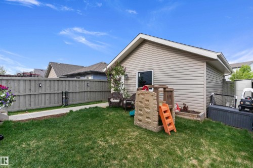 Fenced backyard with a manicured lawn, concrete pathway, and vinyl-sided detached garage featuring a window - 6822 Cardinal Link, Edmonton, AB 