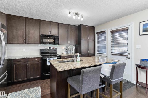 Modern kitchen featuring dark wood-finish cabinetry, granite countertops, and stainless steel appliances - 6822 Cardinal Link, Edmonton, AB 