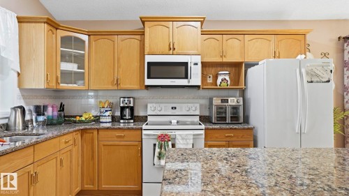 Kitchen featuring wood-finish cabinetry, granite-style countertops, and a white tile backsplash - 856 Graham Wynd, Edmonton, AB 