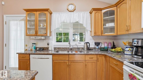 Kitchen featuring light wood cabinetry with glass-front accents, granite countertops, and a white dishwasher - 856 Graham Wynd, Edmonton, AB 
