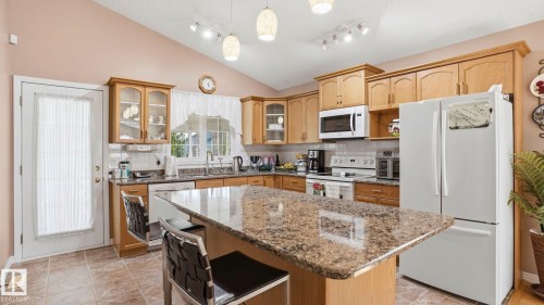 Kitchen featuring a large island with a stone-finish countertop, wood cabinetry, a vaulted ceiling, and recessed lighting - 856 Graham Wynd, Edmonton, AB 