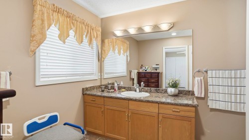 Bathroom featuring a wood-finish vanity with an integrated sink, granite-patterned countertop, and an expansive mirror - 856 Graham Wynd, Edmonton, AB 