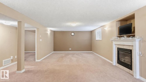 Spacious carpeted room featuring a built-in fireplace with a mantle and tile surround, recessed media niche, and light-toned walls - 856 Graham Wynd, Edmonton, AB 