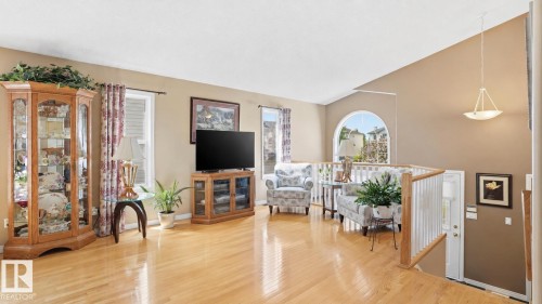 Spacious living area featuring wood-finish flooring, a white spindle railing, and a vaulted ceiling - 856 Graham Wynd, Edmonton, AB 