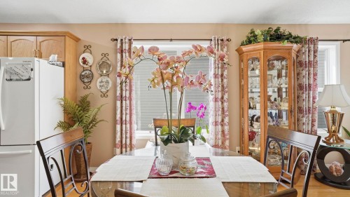 Dining area featuring a glass-top table, wood-finish chairs, and natural light from a window with patterned curtains - 856 Graham Wynd, Edmonton, AB 