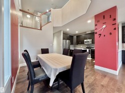 Open-concept living space featuring wood-finish flooring, a contemporary kitchen with dark cabinetry and stainless steel appliances, and a modern glass and wood railing - 