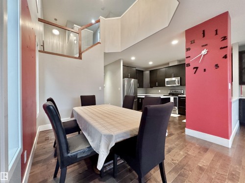 Open-concept living space featuring wood-finish flooring, a contemporary kitchen with dark cabinetry and stainless steel appliances, and a modern glass and wood railing - 3254 Allan Way, Edmonton, AB 