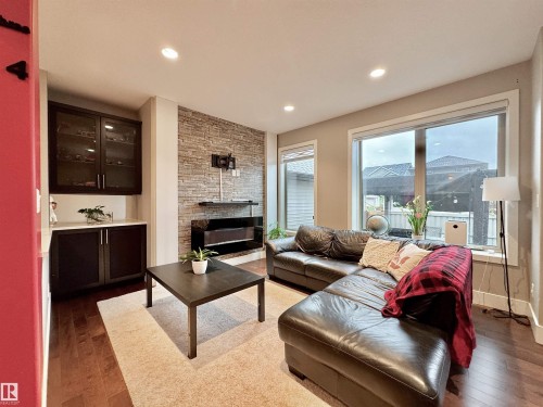 Living area featuring wood-finish flooring, a stacked stone accent wall, and built-in cabinetry with a white countertop - 3254 Allan Way, Edmonton, AB 