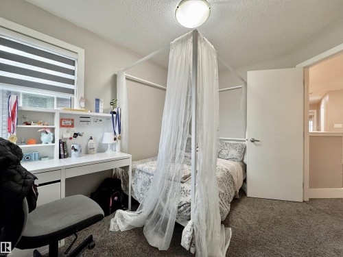 Bedroom featuring a window with horizontal blinds, built-in desk with shelving, gray carpet flooring, and a flush mount ceiling light fixture - 3254 Allan Way, Edmonton, AB 