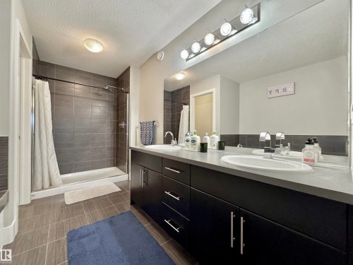 Contemporary bathroom featuring a dark wood-finish double vanity with integrated sinks, a large wall-mounted mirror, and a tiled shower enclosure with a glass door - 3254 Allan Way, Edmonton, AB 