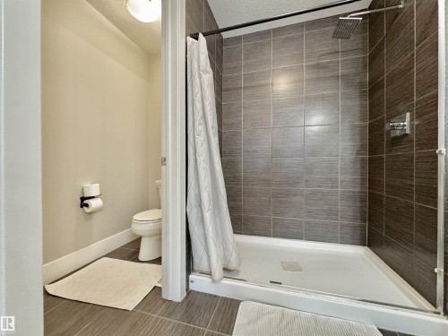 Walk-in shower featuring gray tiled walls, a square rain showerhead, and a white shower pan - 3254 Allan Way, Edmonton, AB 