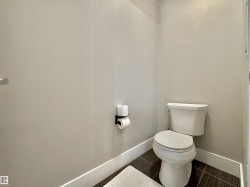 Powder room featuring a white toilet, contemporary dark tile flooring, and white baseboards - 