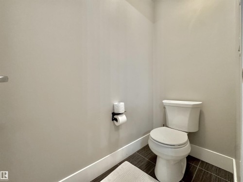 Powder room featuring a white toilet, contemporary dark tile flooring, and white baseboards - 3254 Allan Way, Edmonton, AB 