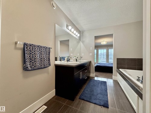 Bathroom featuring a double vanity with undermount sinks and chrome fixtures, ample counter space, a large mirrored wall, and overhead bar lighting - 3254 Allan Way, Edmonton, AB 
