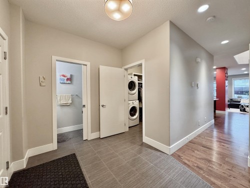 Dedicated laundry area with stacked appliances, featuring ceramic tile flooring and a nearby powder room - 3254 Allan Way, Edmonton, AB 