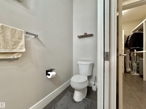 White toilet with a dual-flush mechanism, dark grey floor tiles, white baseboards, and a polished chrome towel bar - 3254 Allan Way, Edmonton, AB 