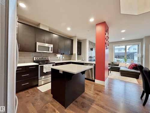Modern kitchen featuring dark wood-finish cabinetry, stainless steel appliances, a white solid-surface island, and wood-finish flooring - 3254 Allan Way, Edmonton, AB 